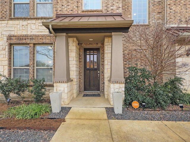 view of exterior entry featuring a standing seam roof, stone siding, metal roof, and brick siding