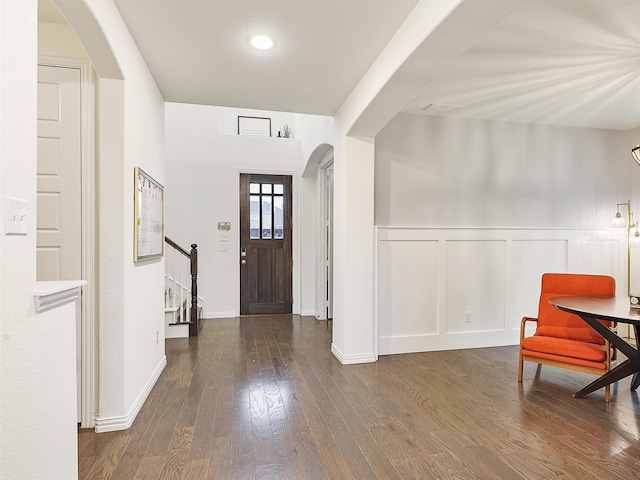 foyer with arched walkways, a wainscoted wall, dark wood finished floors, a decorative wall, and stairs