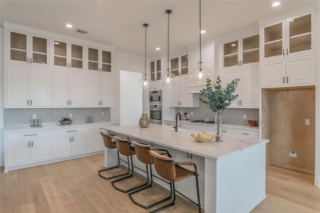 kitchen featuring white cabinets, glass insert cabinets, a center island with sink, and decorative light fixtures