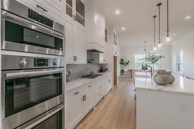 kitchen featuring light stone counters, white cabinets, backsplash, glass insert cabinets, and pendant lighting