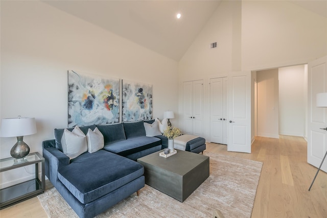 living area with high vaulted ceiling, visible vents, light wood-style flooring, and baseboards