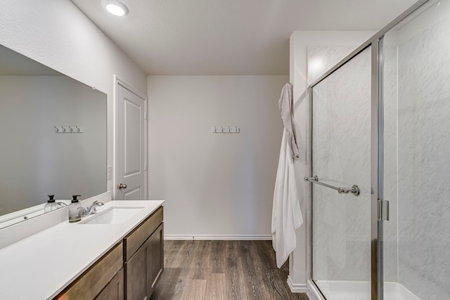 bathroom with baseboards, wood finished floors, vanity, and a shower stall