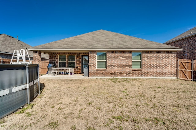 back of property with a patio area, roof with shingles, fence, and brick siding