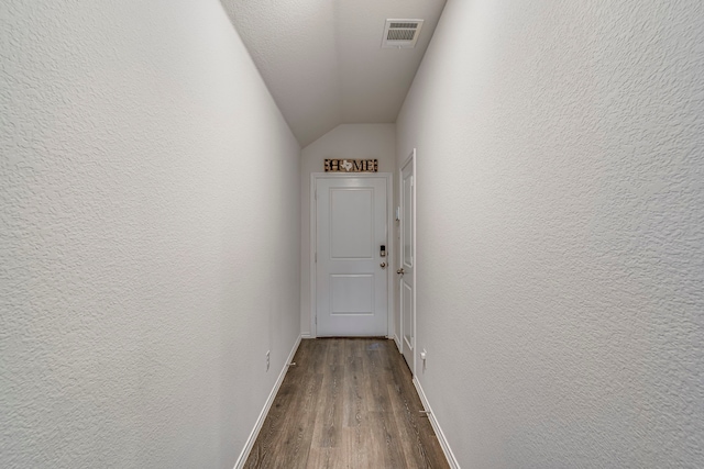 corridor with visible vents, a textured wall, vaulted ceiling, wood finished floors, and baseboards