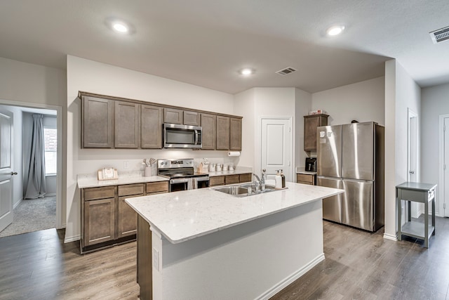 kitchen featuring wood finished floors, a sink, visible vents, appliances with stainless steel finishes, and an island with sink