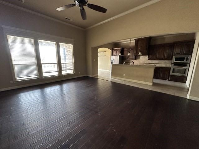 unfurnished living room with arched walkways, baseboards, dark wood finished floors, and crown molding