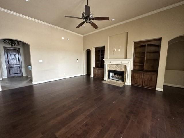 unfurnished living room with baseboards, arched walkways, dark wood finished floors, a ceiling fan, and a premium fireplace