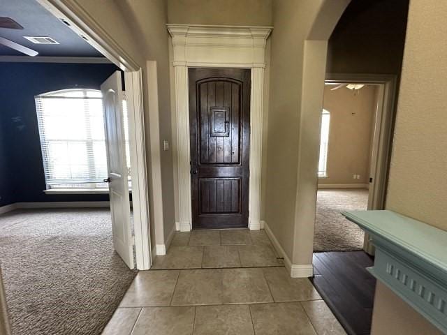 entrance foyer with arched walkways, visible vents, light carpet, and a ceiling fan