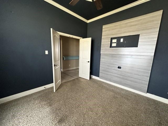 unfurnished bedroom with carpet floors, ceiling fan, baseboards, and crown molding