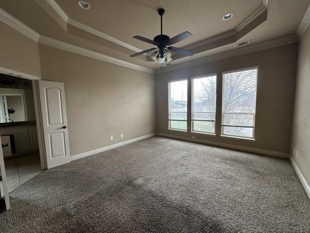 unfurnished bedroom with ornamental molding, a tray ceiling, carpet flooring, and baseboards