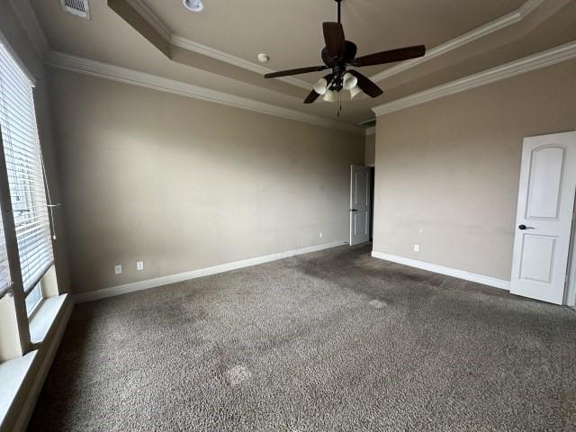 spare room with ornamental molding, dark colored carpet, a raised ceiling, and baseboards