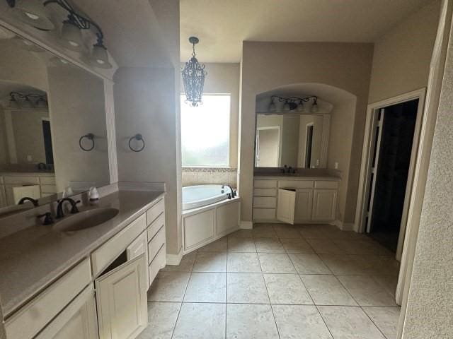 bathroom with a garden tub, a notable chandelier, two vanities, a sink, and tile patterned floors