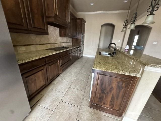 kitchen featuring arched walkways, pendant lighting, black electric stovetop, a sink, and light stone countertops