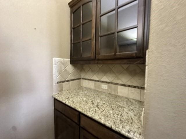 kitchen with glass insert cabinets, light stone counters, backsplash, and dark brown cabinets