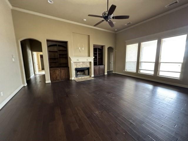 unfurnished living room featuring arched walkways, a fireplace, visible vents, ornamental molding, and dark wood-style floors