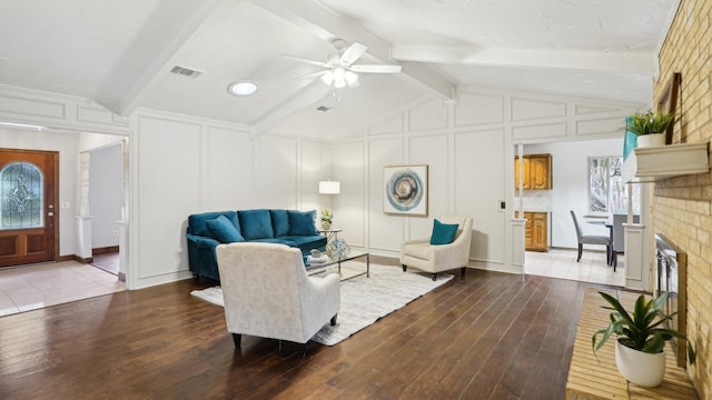 living room featuring lofted ceiling with beams, a fireplace, wood finished floors, and a decorative wall