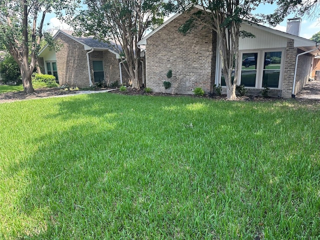 view of front of home featuring brick siding, a chimney, and a front lawn