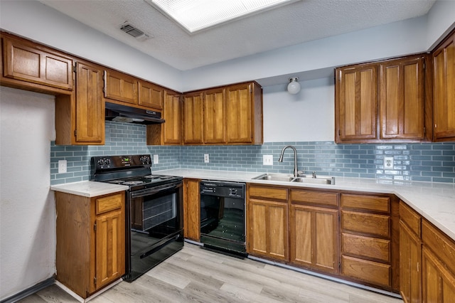 kitchen with light countertops, brown cabinetry, a sink, under cabinet range hood, and black appliances