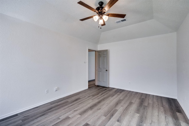 spare room with wood finished floors, visible vents, baseboards, vaulted ceiling, and a ceiling fan