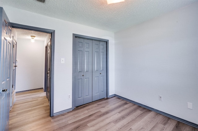 unfurnished bedroom with a closet, baseboards, a textured ceiling, and light wood finished floors