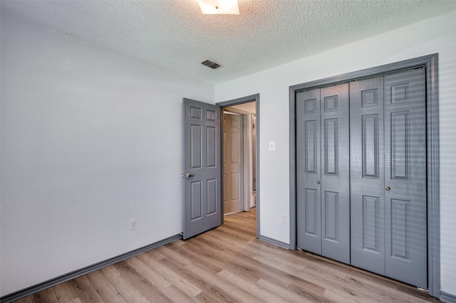 unfurnished bedroom with a textured ceiling, visible vents, baseboards, light wood-style floors, and a closet