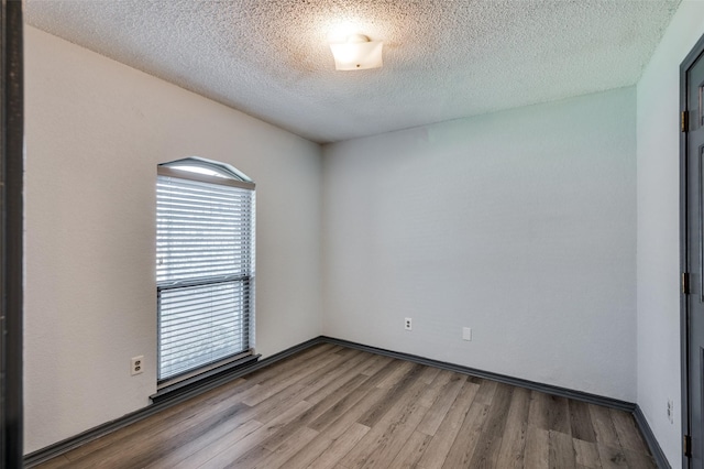 empty room featuring a textured ceiling, baseboards, and wood finished floors