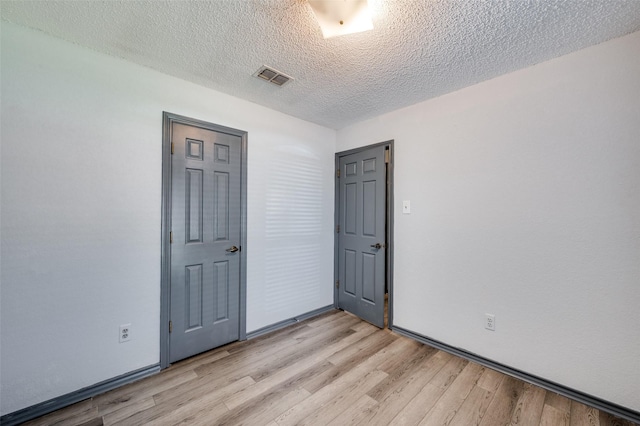 unfurnished room with light wood-style flooring, visible vents, and a textured ceiling