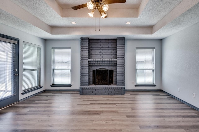 unfurnished living room featuring a brick fireplace, a textured ceiling, a raised ceiling, and wood finished floors