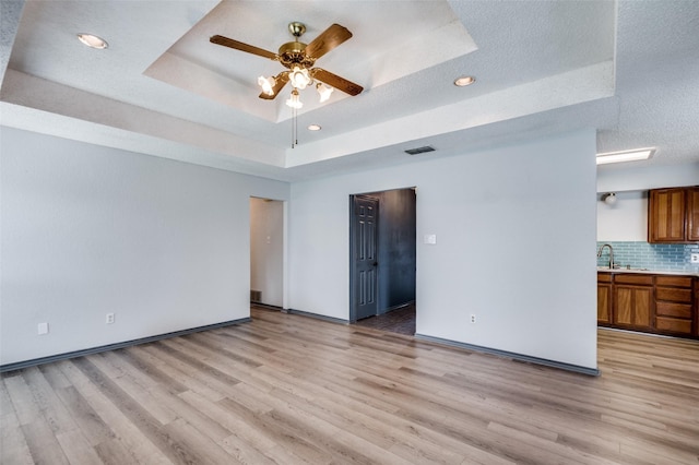 unfurnished room with a tray ceiling, visible vents, ceiling fan, and light wood finished floors