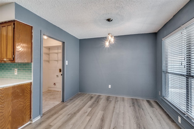 unfurnished dining area featuring a textured ceiling, light wood finished floors, and baseboards