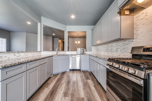 kitchen featuring light wood finished floors, decorative backsplash, a peninsula, light stone countertops, and stainless steel appliances