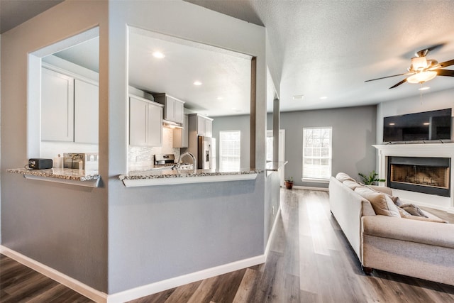 kitchen with a peninsula, white cabinets, open floor plan, stainless steel refrigerator with ice dispenser, and light stone countertops