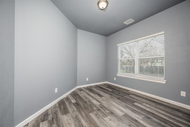 spare room with wood finished floors, visible vents, and baseboards