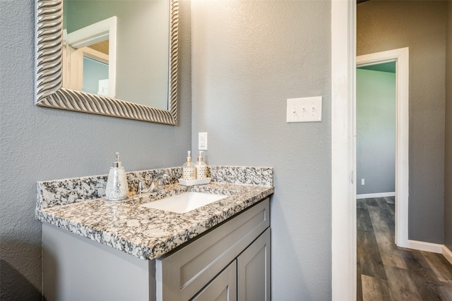 bathroom with a textured wall, vanity, baseboards, and wood finished floors