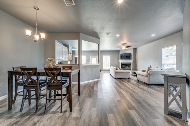 dining room with a fireplace, visible vents, wood finished floors, baseboards, and ceiling fan with notable chandelier