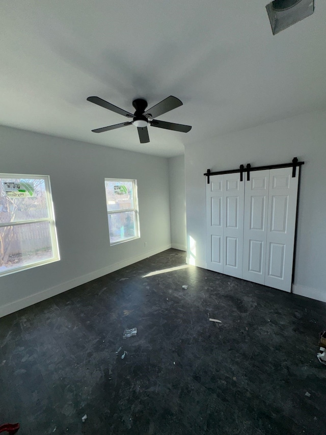 empty room featuring a barn door, baseboards, and ceiling fan