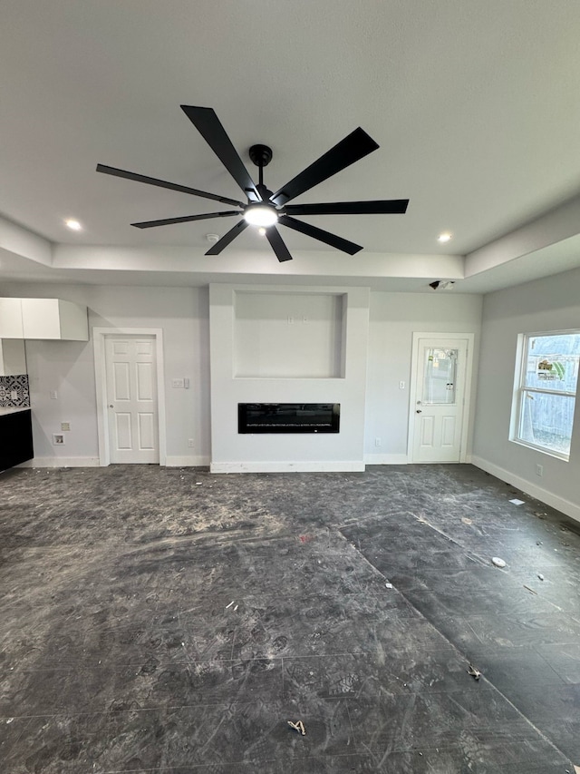 unfurnished living room with recessed lighting, baseboards, a tray ceiling, and a glass covered fireplace