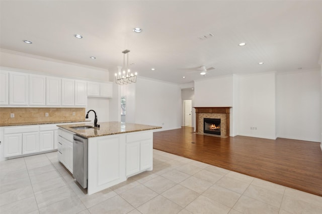 kitchen featuring a center island with sink, hanging light fixtures, stainless steel dishwasher, open floor plan, and white cabinetry