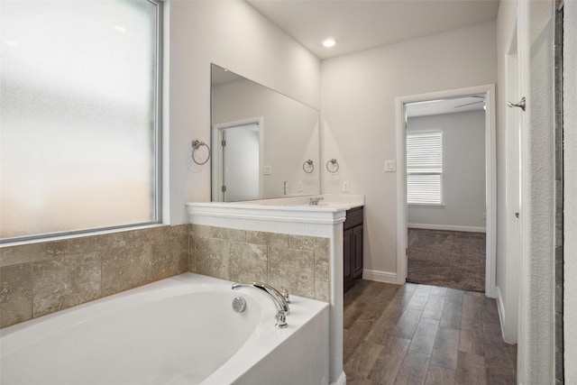 bathroom featuring a bath, baseboards, wood finished floors, and vanity