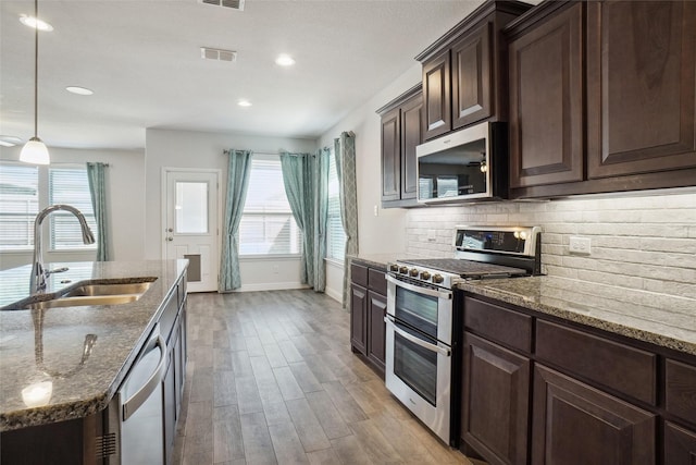 kitchen featuring decorative light fixtures, stainless steel appliances, decorative backsplash, a sink, and light stone countertops