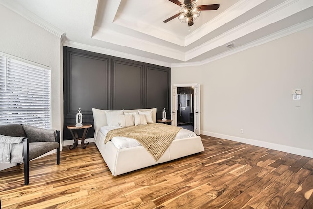 bedroom featuring baseboards, light wood finished floors, a raised ceiling, and crown molding