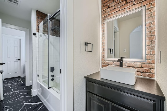 full bathroom with visible vents, bath / shower combo with glass door, brick wall, marble finish floor, and vanity