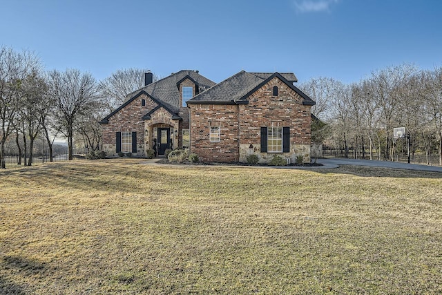 french country home with brick siding, a chimney, stone siding, and a front yard