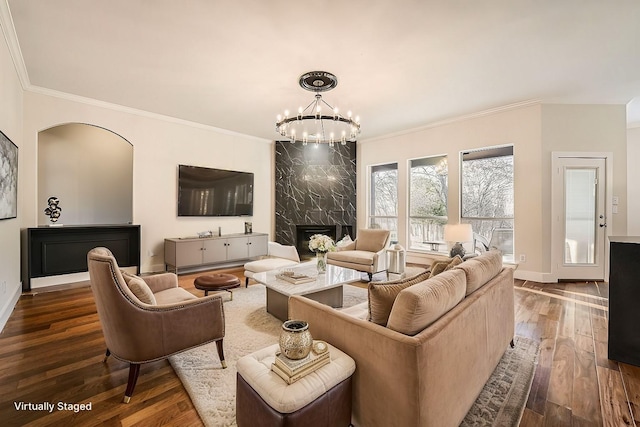 living area with baseboards, hardwood / wood-style floors, crown molding, a fireplace, and a chandelier