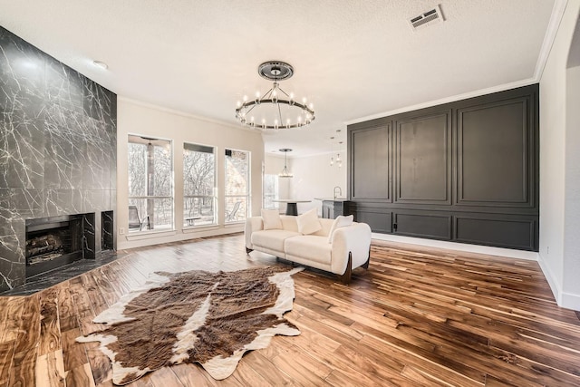 living room with wood finished floors, an inviting chandelier, crown molding, a textured ceiling, and a high end fireplace