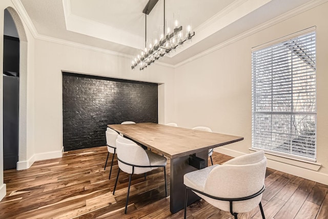 dining room with a tray ceiling, crown molding, baseboards, and wood finished floors