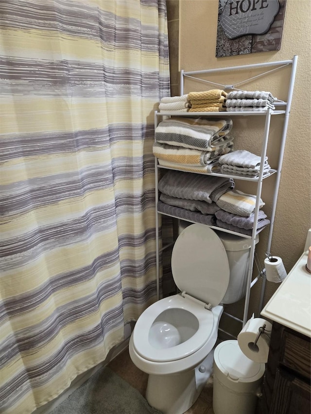 full bath featuring toilet, a textured wall, and vanity