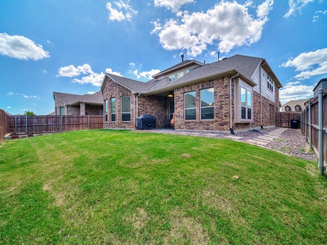 back of property featuring brick siding, a lawn, and a fenced backyard