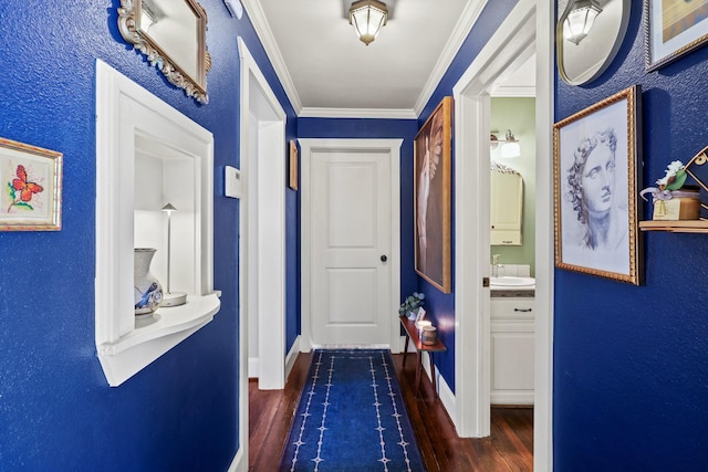 hallway with dark wood-type flooring, a sink, crown molding, and baseboards