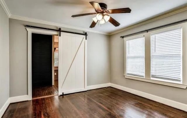 spare room with a barn door, a ceiling fan, baseboards, dark wood-style floors, and crown molding